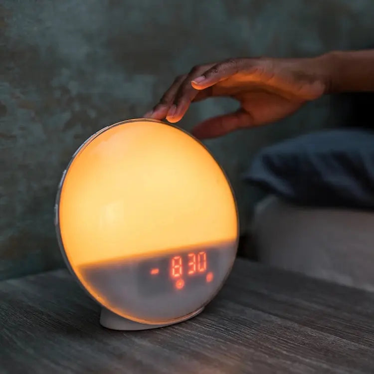 réveil circadien sur table de nuit avec un main qui appuie dessus 